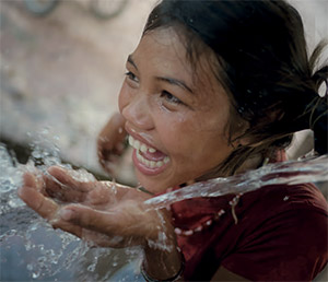 Uma rapariga sorri enquanto bebe água, na República Democrática Popular do Laos, em 2015. © UNICEF/UNI182989/NOORANI